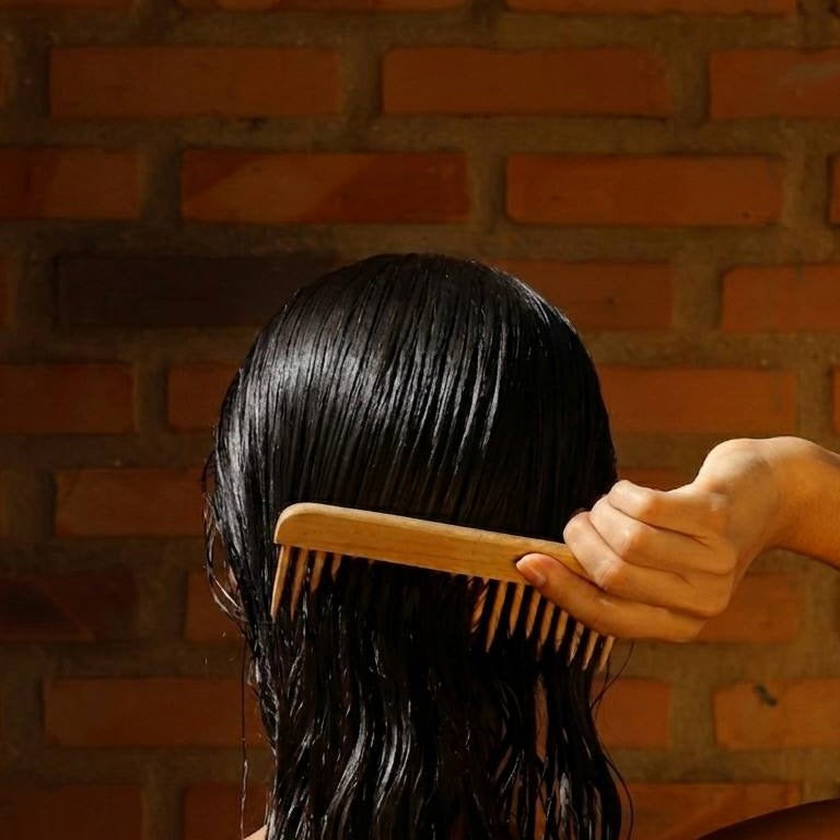 Mulher penteando cabelo molhado, parede de tijolos ao fundo